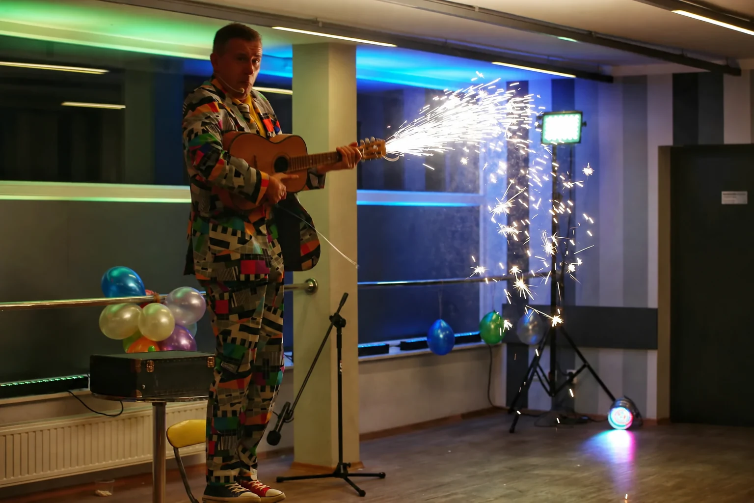 Bogdan Michalec z gitarą emitującą iskry w oświetlonej sali.