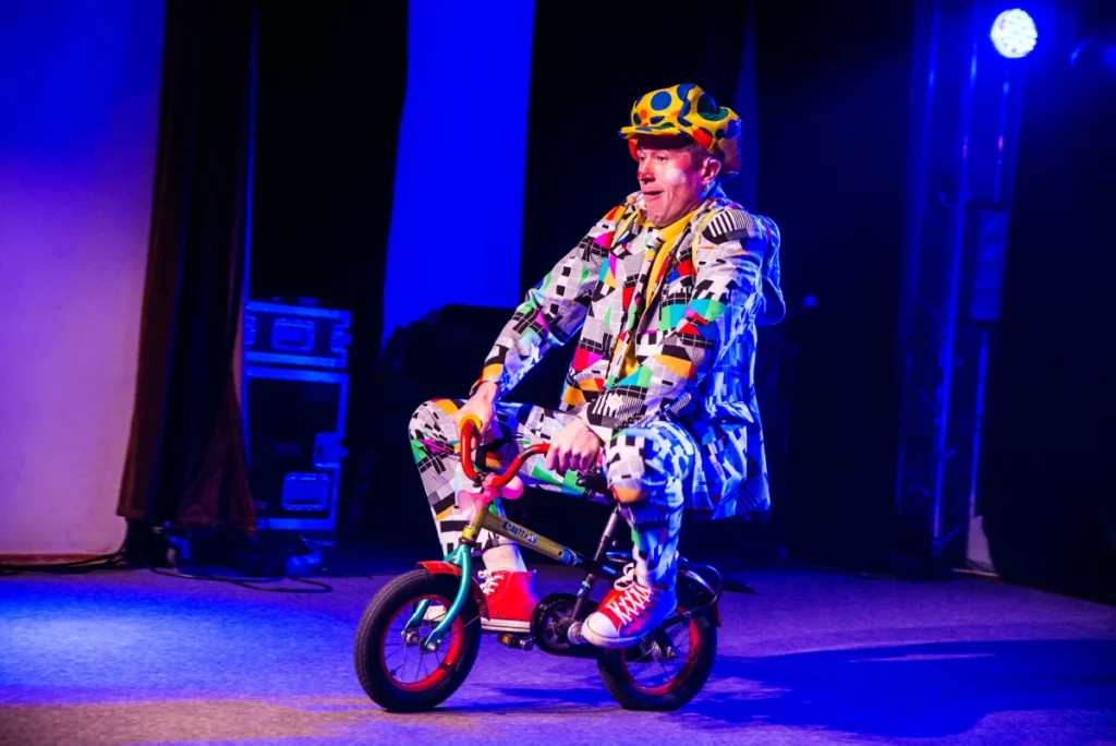 Bogdan Michalec podczas eventu firmowego wykonuje komediowy numer na małym rowerku